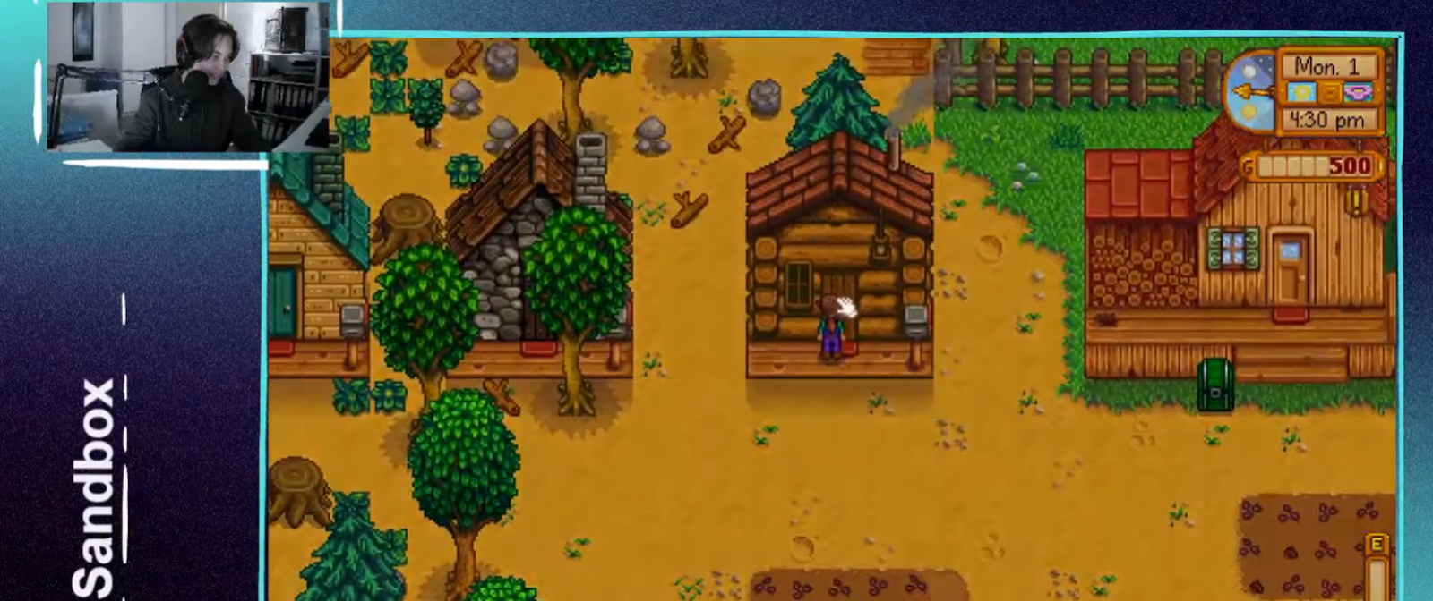 Ein Bildschirm mit einer Szene aus einem Computerspiel mit altmodischer Grafik. Eine Figur steht darin vor einem der vielen einfachen Holz- und Steinhäuser. Links oben auf dem Bildschirm ist eine Person, vermutlich der Spieler, mit Headset zu sehen. 