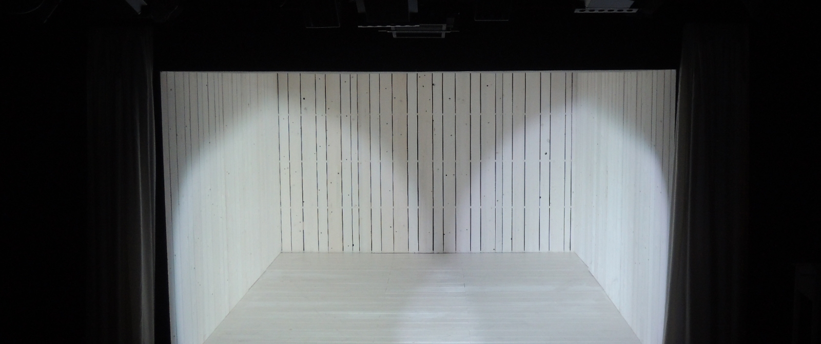Auf einer Bühne steht eine nach vorne geöffnete Box, die mit weißen Holzpaneelen ausgekleidet ist. 