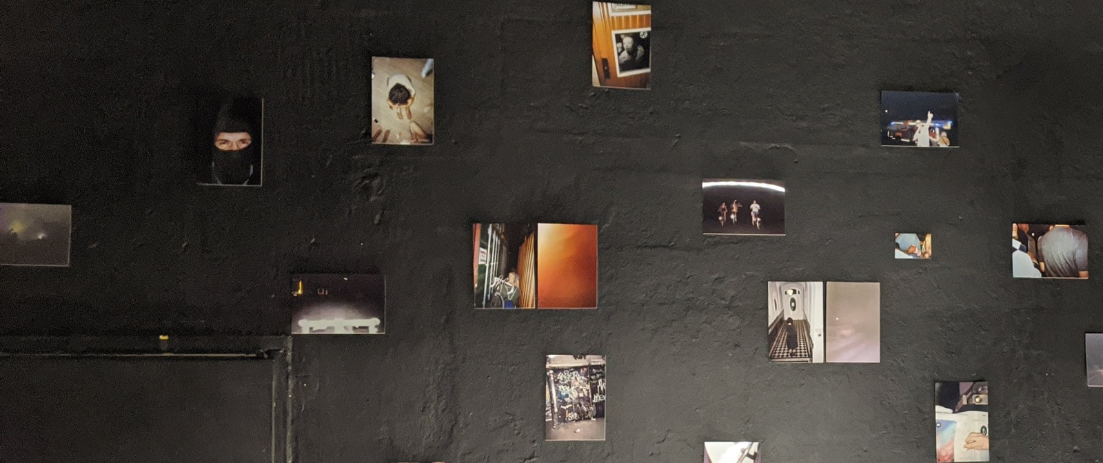 Eine schwarze Wand mit mehreren Fotografien in dunklen Tönen.