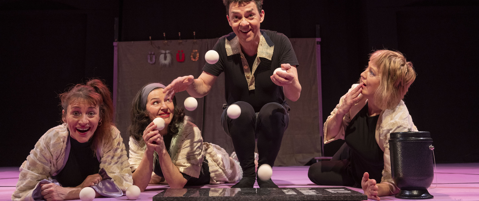 Vier Personen in einer Reihe, drei ligen auf dem Bauch und schauen Richtung Kmaera, die zweite von rechts hockt und jongliert vier weiße Bälle auf dem Boden.