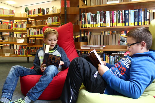 Zwei Jungs sitzen in Sitzsäcken vor Bücherregalen und lesen.