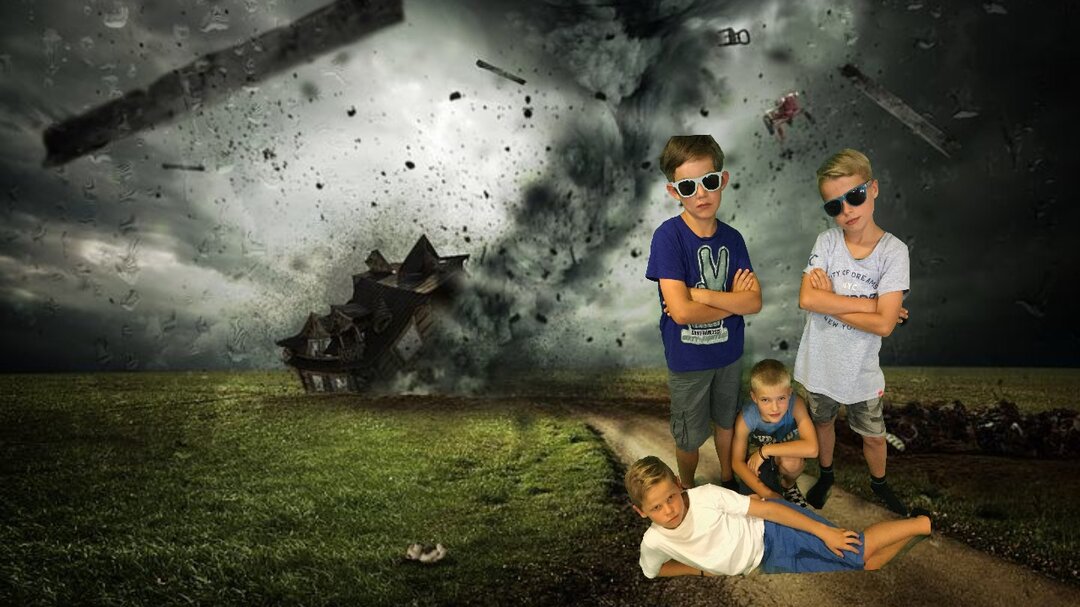 Vier Kinder stehen vor einem Greenscreen. Der Greenscreen stellt einen Feldweg mit einem Tornado im Hintergrund dar. Zwei der vier Kinder stehen und haben die Arme verschränkt und Sonnenbrillen auf. Ein Kind liegt seitlich vor ihnen. Das andere Kind kniet zwischen den beiden stehenden Kindern.