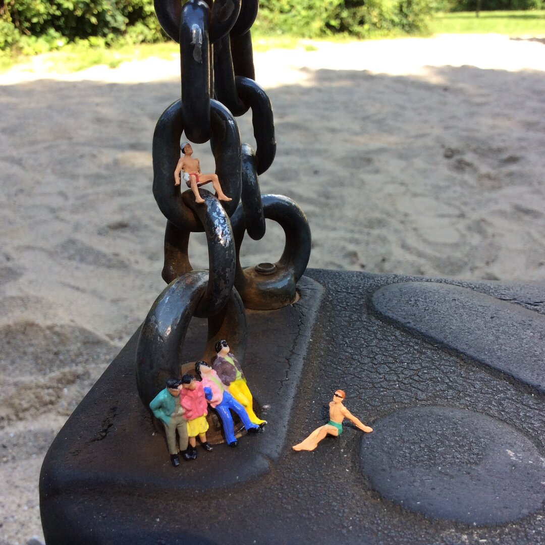 Miniatur-Figuren stehen auf einer Schaukel.